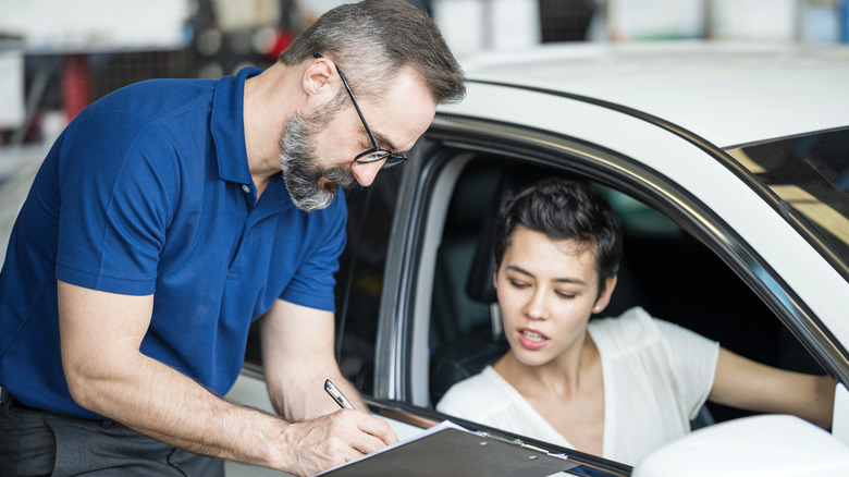 a male auto technician consulting with a female client in a white car
