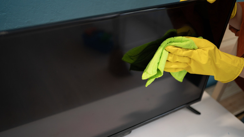 Gloved hand cleans TV with cloth