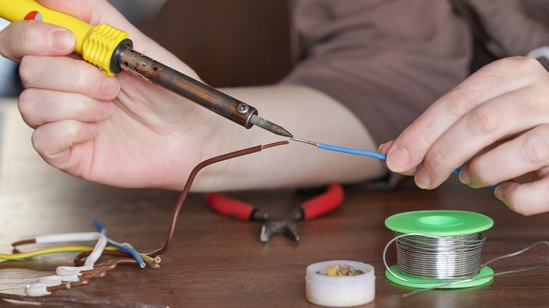 Close-up of person holding soldering iron to a tinned wire