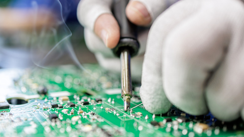 Close up of gloved hands soldering a printed circuit board