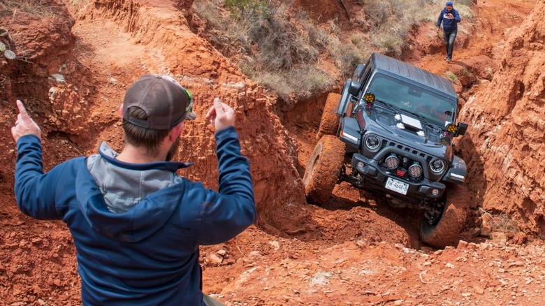 An off-road driver taking direction from a spotter to negotiate difficult terrain.