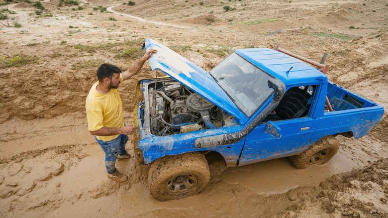 A man looking at his truck's engine while off-roading.