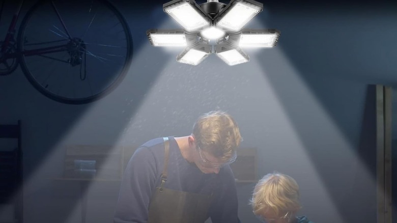 A man and son next to each other working on something with garage lights up.