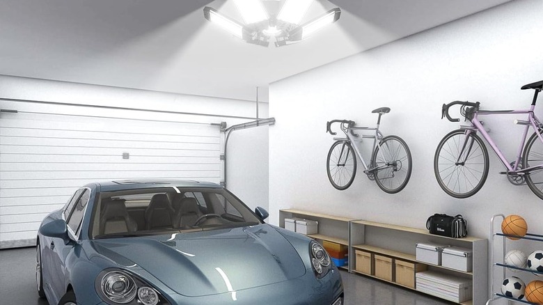 A garage light over a blue car with bikes on the wall.