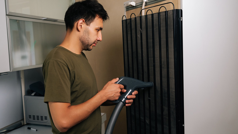 Man vacuuming the condenser coils on the back of a refrigerator.