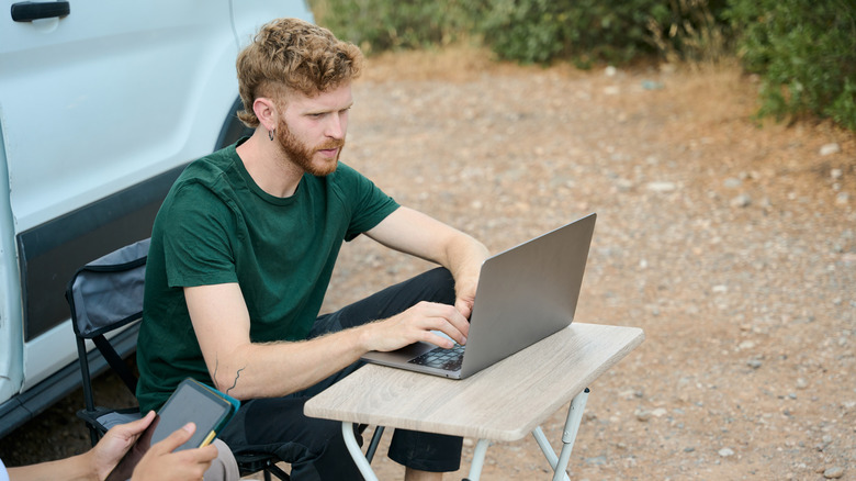 young man working on laptop in remote campsight