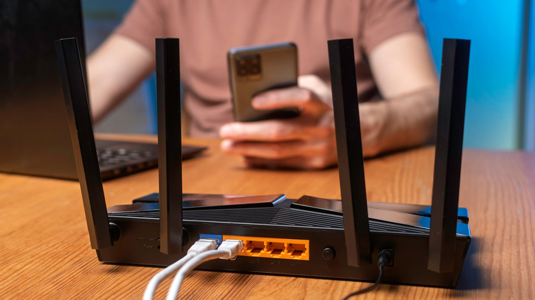 A man sitting at a computer with a smartphone with a Wi-Fi router in the foreground