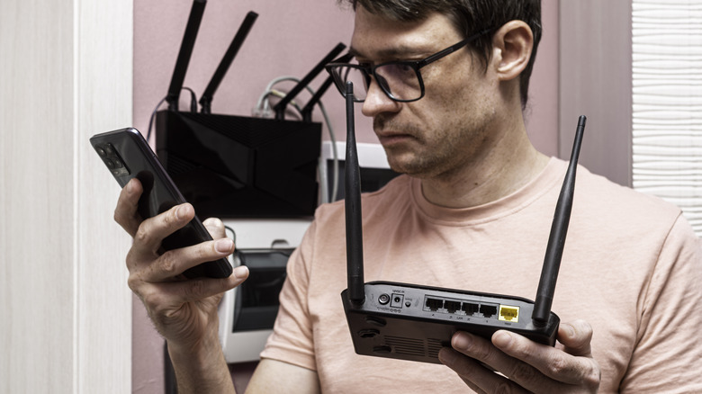 A man with a smartphone holding a router and diagnosing it