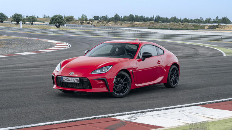 A red Toyota GR86 on a race track, front 3/4 view, static shot