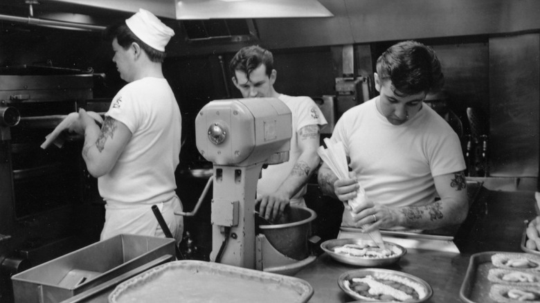 Three cooks preparing meals aboard the galley of a British submarine