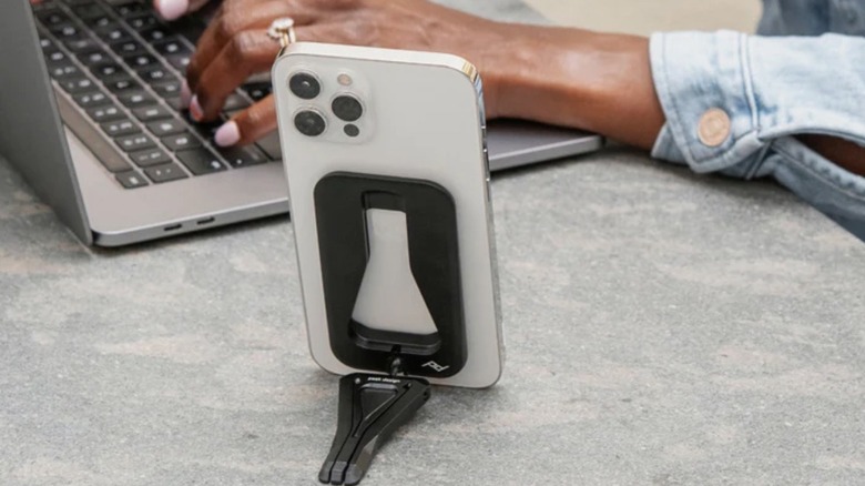 Mobile tripod holding a phone while a person works on laptop