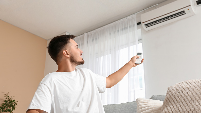 A man turning on a wall-mounted air conditioner.