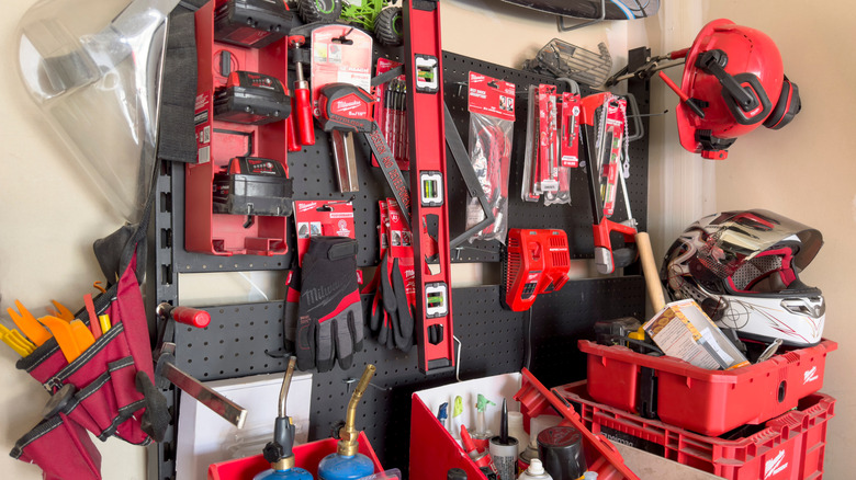 Assortment of red and black tools by Milwaukee hanging on a black peg board in garage