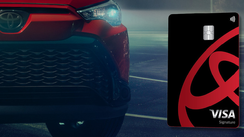 A Toyota credit card next to the front grille of a red Toyota.