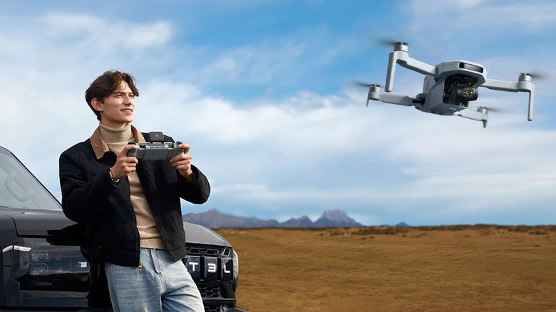 Man piloting a Potensic ATOM 2 Drone in an open field near mountains.