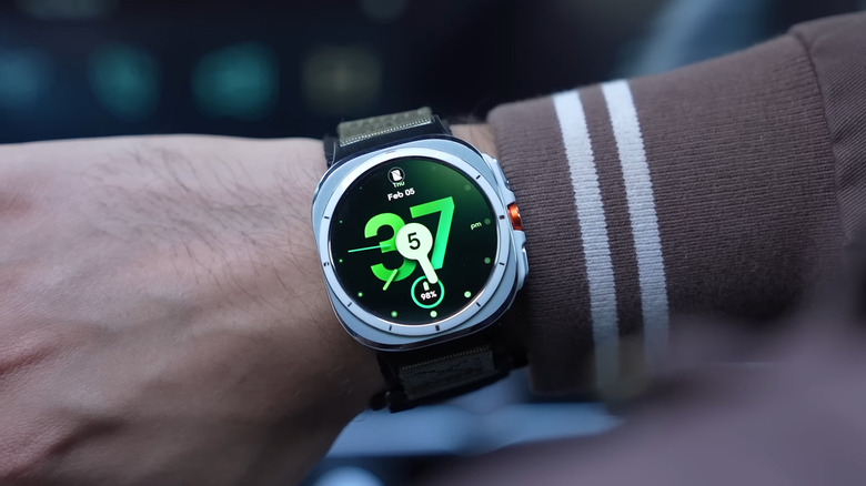 A hand in a full-sleeve garment wearing a Galaxy Watch Ultra from the first generation with a neo-modern watch face visible.