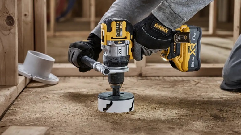 A worker wearing safety gloves using a DeWalt 1/2-Inch Hammer Drill on a subfloor