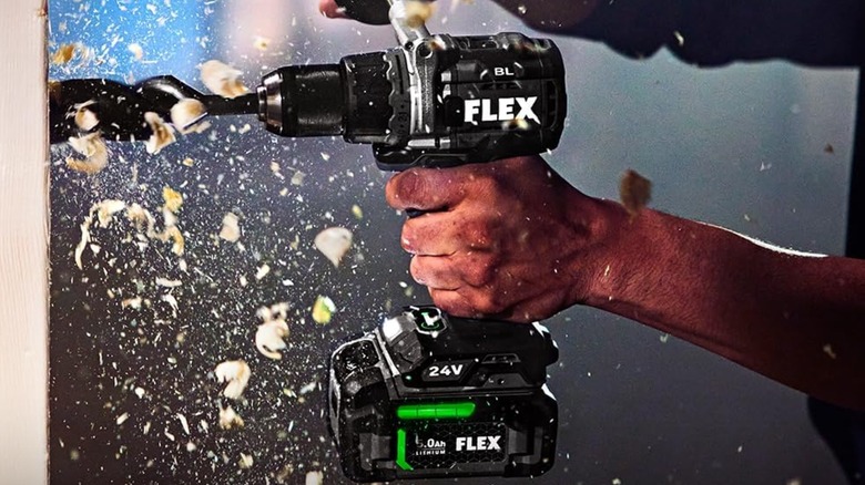 A person using a Flex hammer drill on a vertical wooden surface