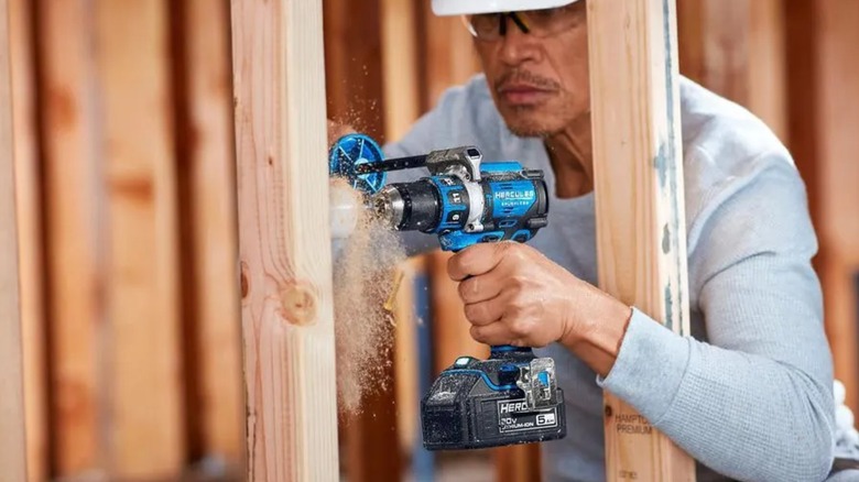 A worker wearing eye and head protection drilling into a wall stud with a Hercules hammer drill