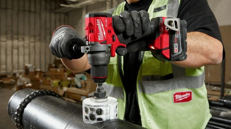 A worker using a Milwaukee hammer drill and a hole saw to cut metal pipe