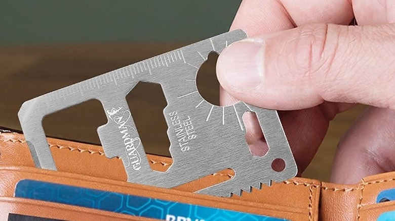 A person pulling a Guardman 11-in-1 Survival Card out of their wallet.