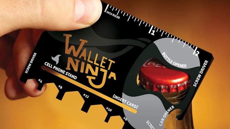 A person using the Wallet Ninja Multitool Card to open a bottle.