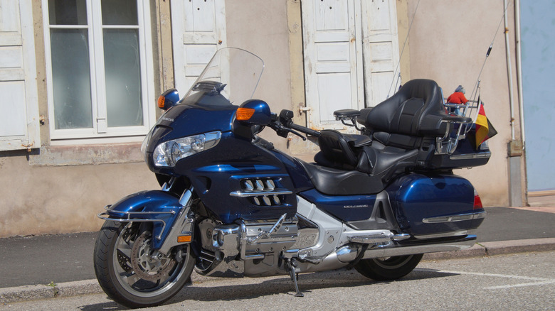 A blue Honda Gold Wing motorbike parked upright on a street outside a beige building.