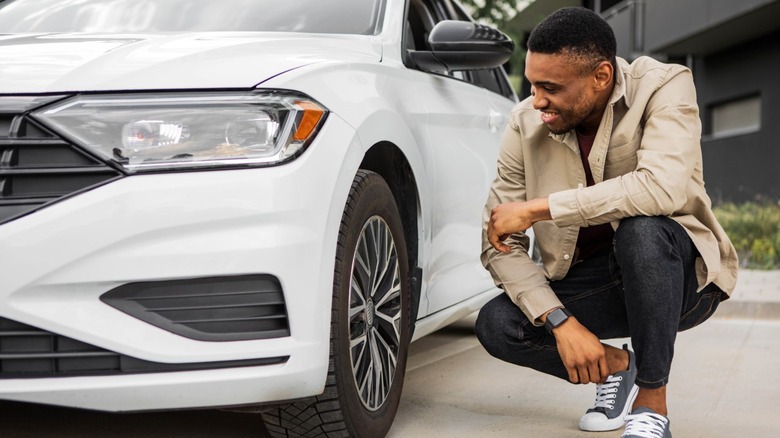 A person looking at their car's tires, smiling.