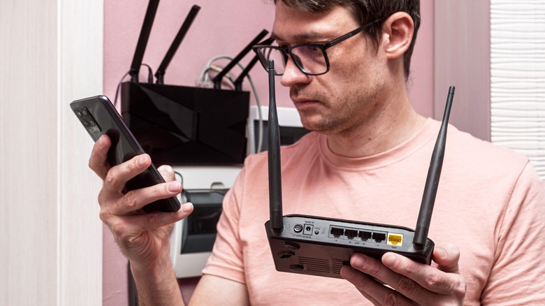 A man at home holding a Wi-Fi router and a smartphone