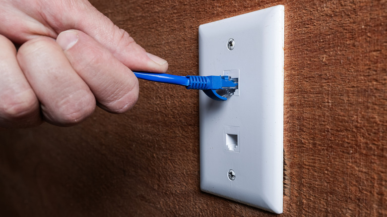 A close up of a hand plugging a Ethernet cable into a RJ45 wall jack