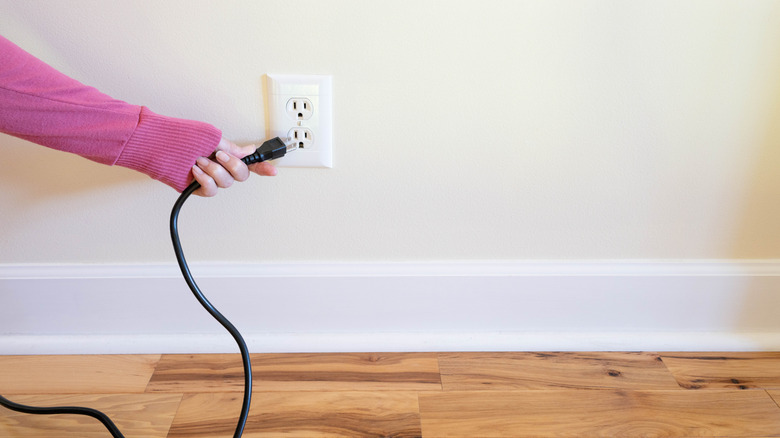 A person disconnecting a power cord from a wall outlet