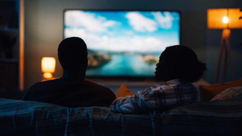 A couple watching TV with a bright scene on the screen