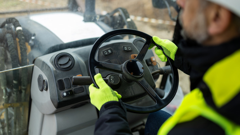 A person holding a backhoe's steering wheel in both hands.