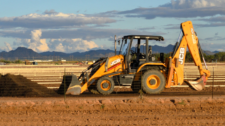 A yellow backhoe loader positioning its front bucket to scoop up soil.