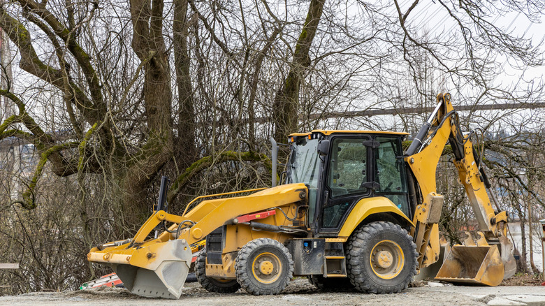 A yellow backhoe loader parked beside a tree in a snowy area.