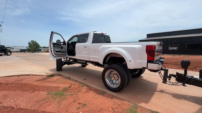 A lifted white pickup truck with the driver side door open, attached to a trailer in a suburban driveway.
