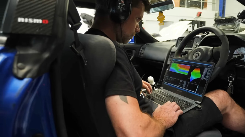 A man sitting in the driver's seat of a car with a laptop open, running ECU tuning software.