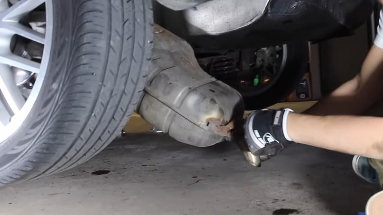 A man wearing gloves removing the muffler off a vehicle after having cut the pipe.