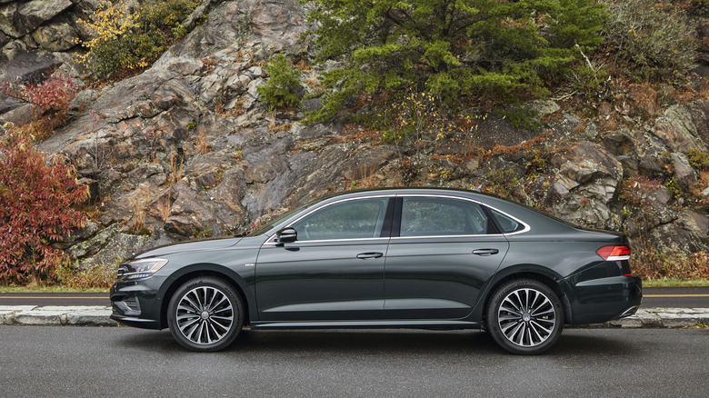 Dark green 2022 Volkswagen Passat sedan seen from directly left parked in front of a rocky hill