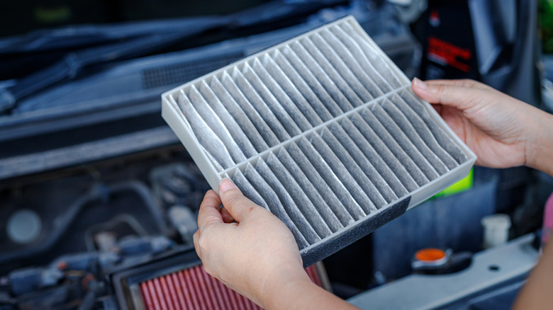 Close-up of person inspecting old air filter with new air filter resting beside engine bay