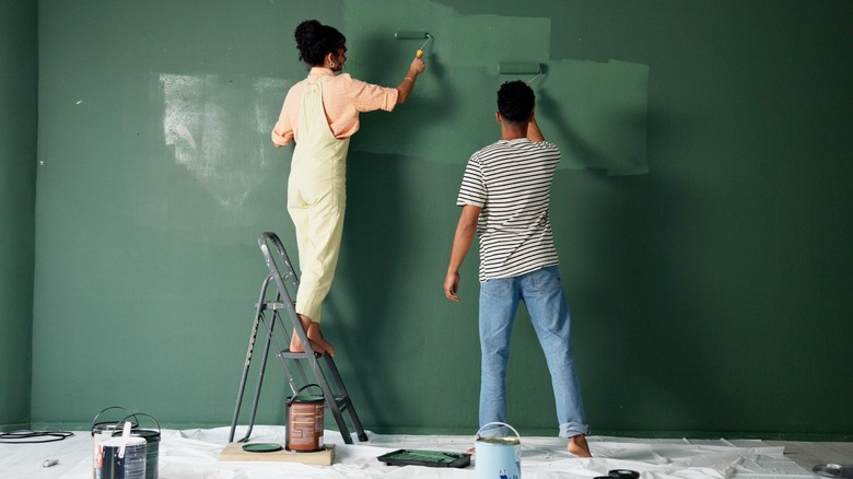 Two people using rollers to paint a wall green
