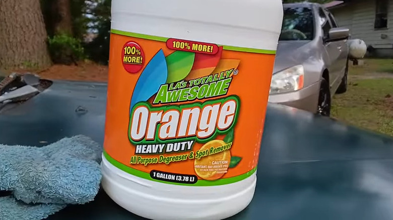 Bottle of orange degreaser on a car hood with towel nearby