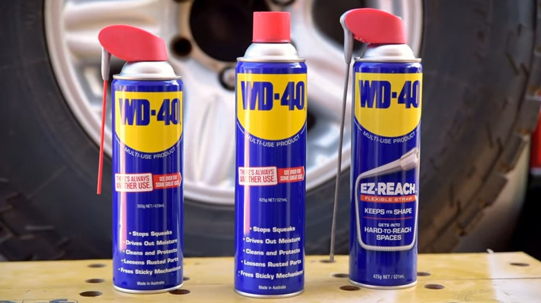 Three cans of WD-40 on a table in front of a wheel