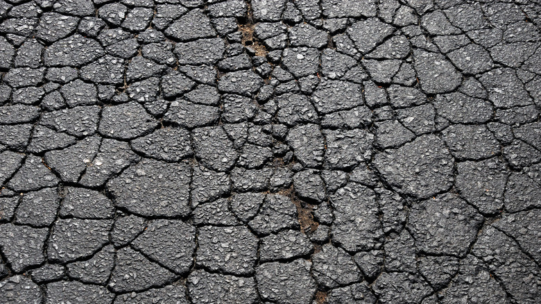 Heavily cracked black asphalt. with a few dirt patches exposed beneath.