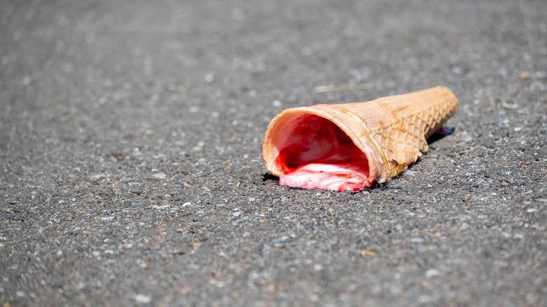 An ice cream cone melting on hot black asphalt.