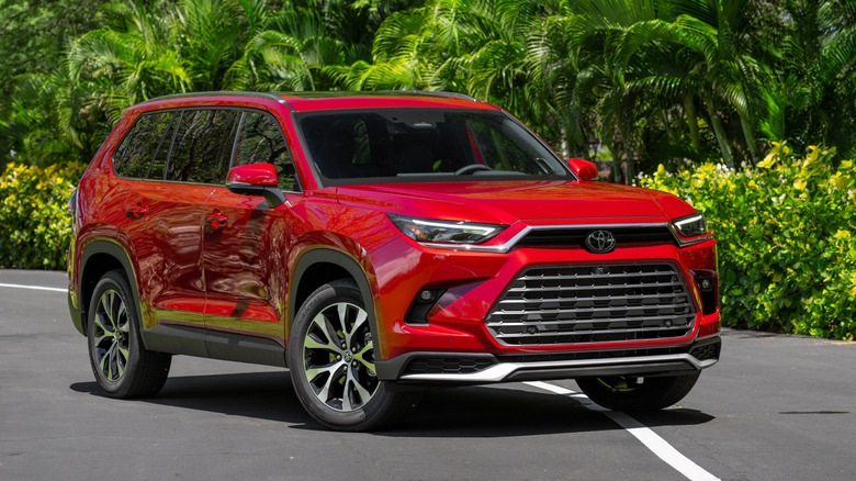 Front 3/4 view of red Toyota Grand Highlander parked in front of bushes.