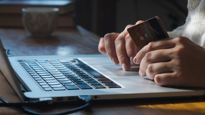 A person holding a credit card while using a laptop