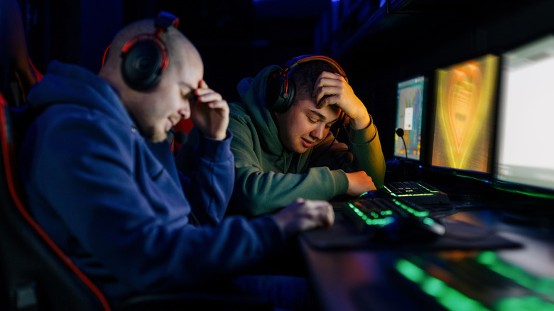 Two gamers sitting in front of their PCs with frustrated expressions