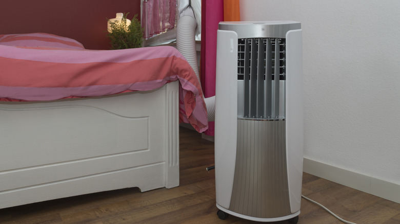 Portable air conditioner in a bedroom with a long vent hose attached to a window