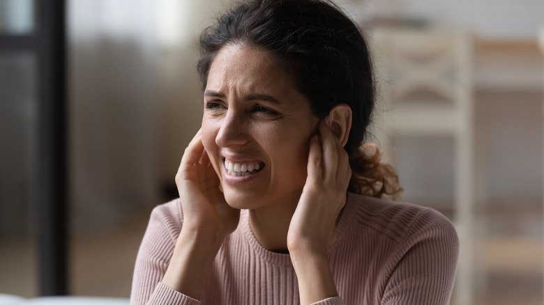 A woman holding her ears and grimacing as a result of a loud noise